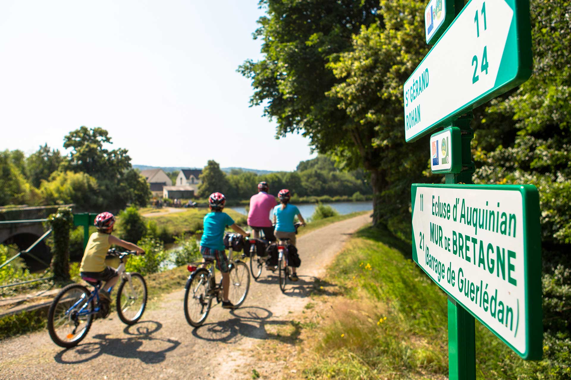 Famille à vélo passant devant des panneaux d'indication de véloroutes