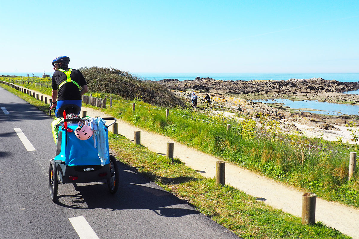 Un cycliste tire une remorque enfant sur la route en front de mer