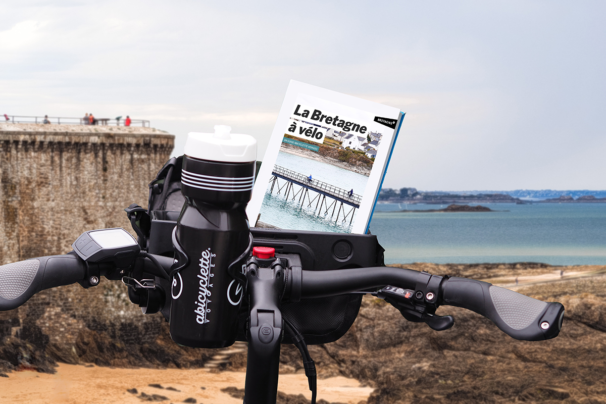 Guide "la Bretagne à vélo" dans la sacoche avant d'un vélo avec vue sur la baie de Saint Malo