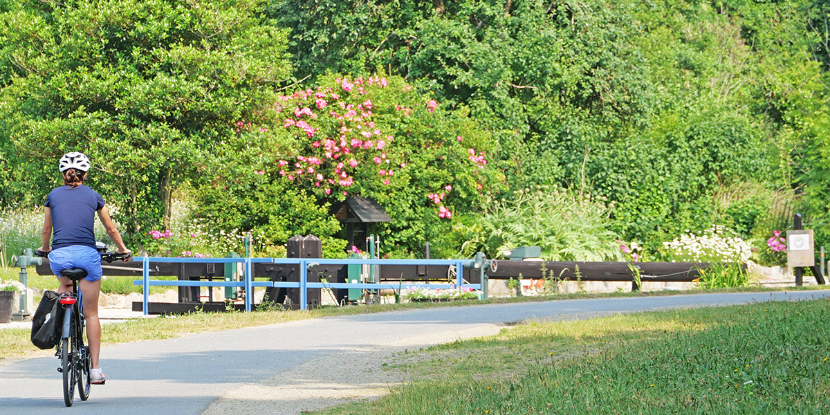 A cyclist rides along the towpath past a flower-bedecked lock