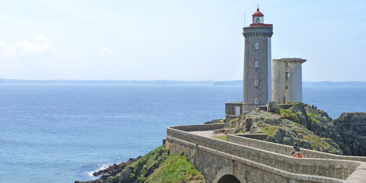 Cycliste rouant sur la route sinueuse d'un phare breton