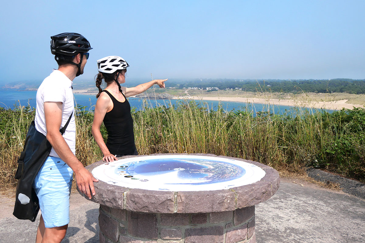 Deux cyclistes consultent une table d'orientation avec vue sur la côte bretonne