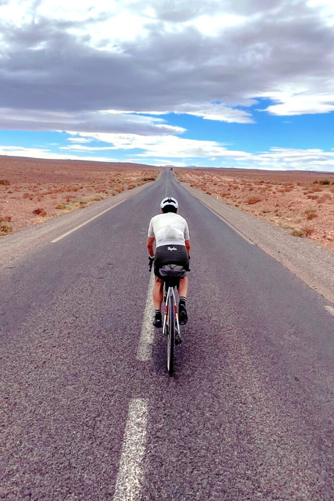 Cycliste sur un route goudronnée droite à travers le désert marocain