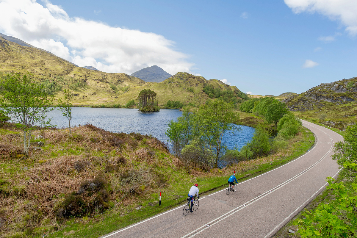 Two cyclists on the roads of Scotland, surrounded by lakes and mountains.