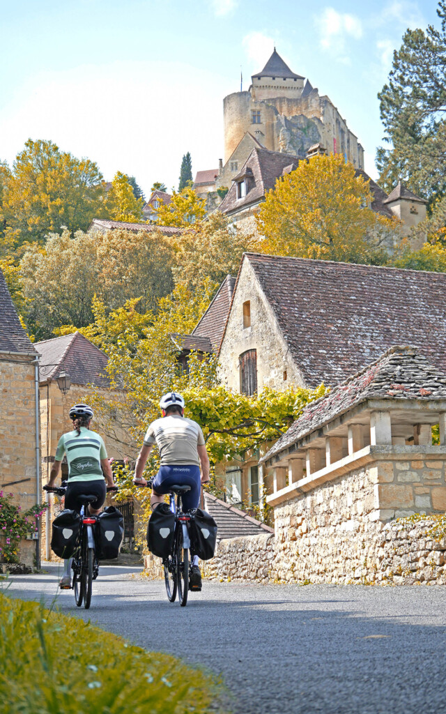 Deux cyclistes de dirigeant vers un château surplombant un petit village aux couleurs automnales