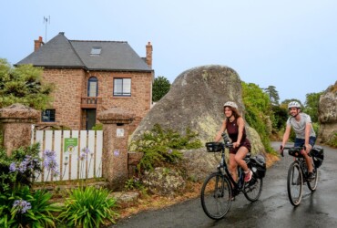 Un couple de cyclistes traverse un peitt hamaux avec des maisons aux pierres roses