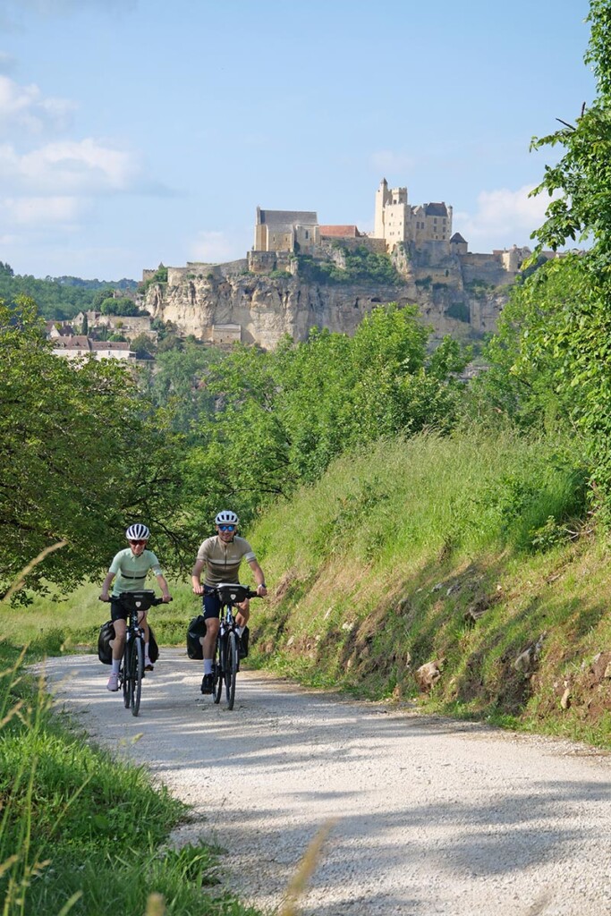 Un couple de cycliste roule sur un chemin avlloné avec un paysage de foret derrière eux