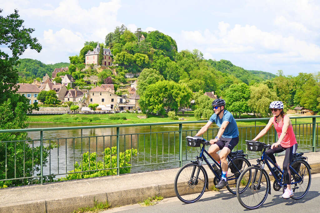 Two cyclists cross a bridge overlooking a medieval city