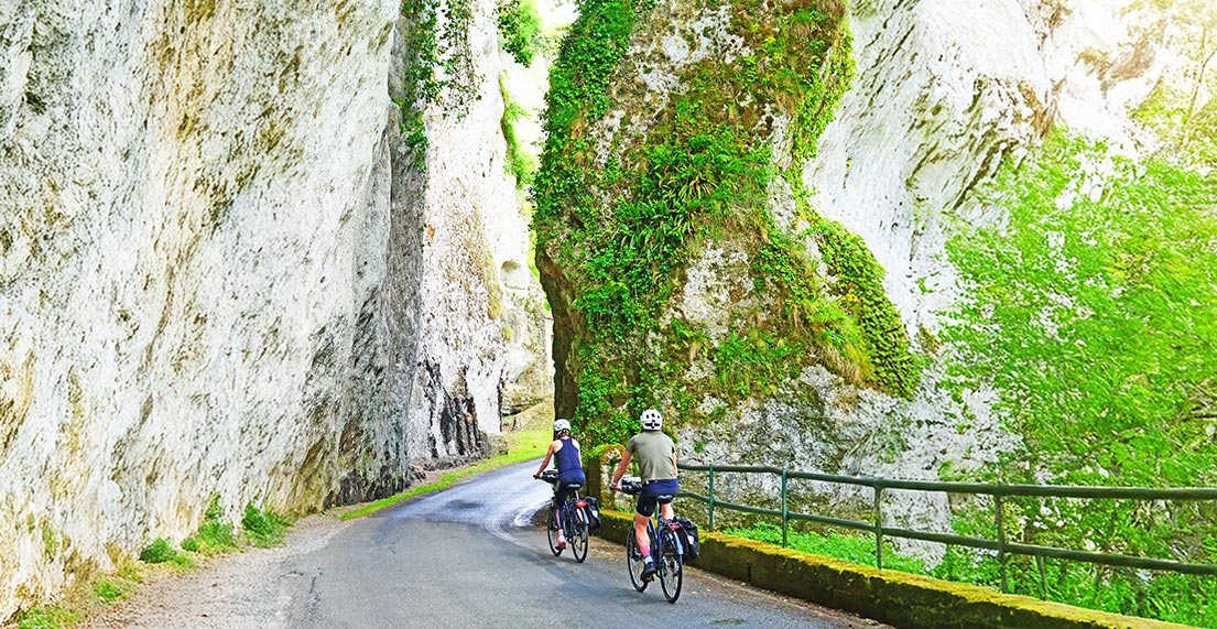 Un couple de cycliste roule devant les falaise de calcaire des Eyzies