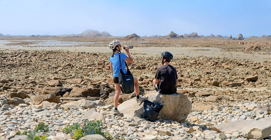 Un couple de cycliste fait une pause fraicheur sur une plage de rochers roses
