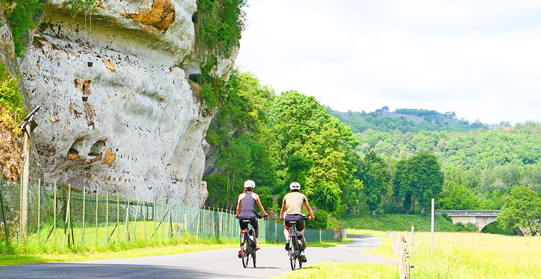Un couple de cycliste roule devant les falaise de calcaire des Eyzies