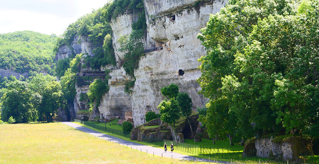 Un couple de cycliste roule devant les falaise de calcaire des Eyzies