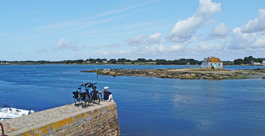Un couple de cyclistes admire la maison entourée d'eau de Saint Cado