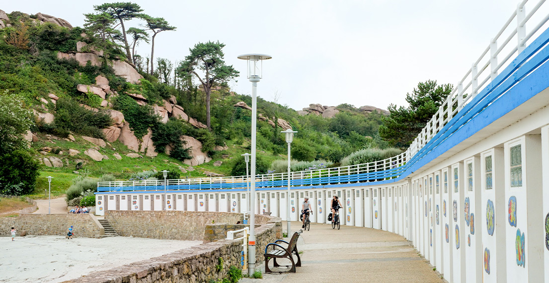 Un couple de cyclistes roule le long de cabanes de plage blanches