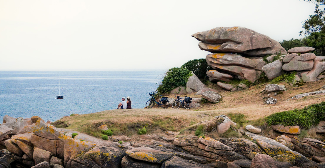 Un couple de cycliste est assis devant la mer entoures de rochers roses