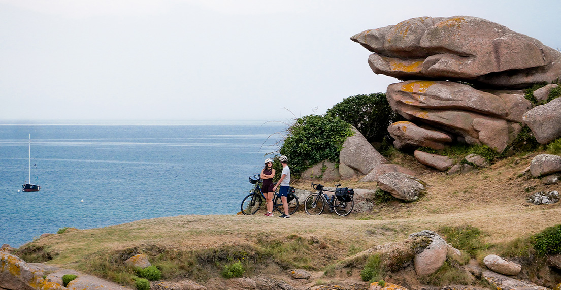 Un couple de cyclistes devant un rocher rose et train d admirer la mer