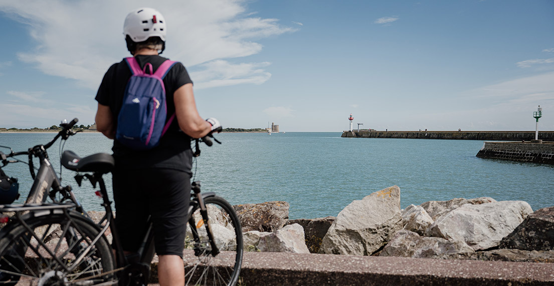 Une cycliste regarde la mer en direction d'un phare