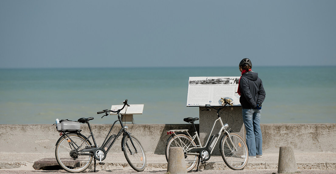 Une cycliste lit un panneau d'information en front de mer