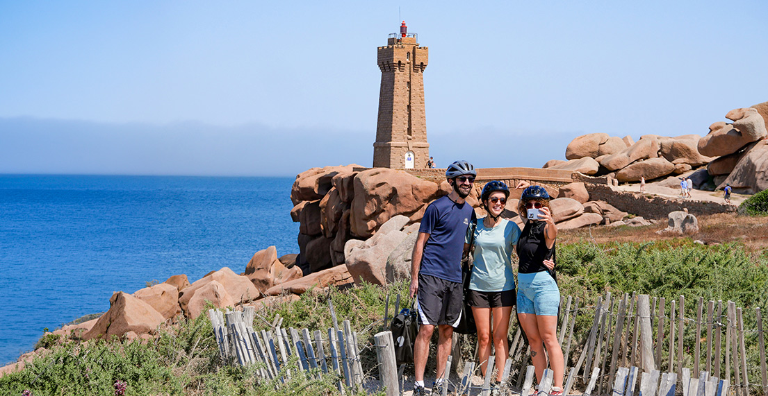 Trois cyclistes se prennent en photo devant le phare rose de Ploumanach