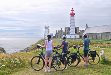 Trois cyclistes regardent en direction du phare blanc et rouge Saint-Mathieu
