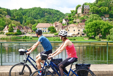 Deux cyclistes sur un pont avec vue sur une citée médiévale