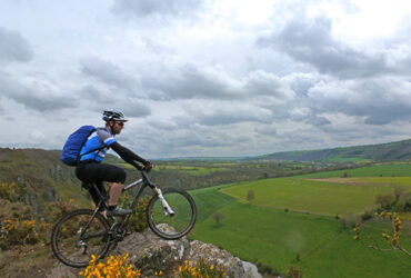 Un cycliste surplombe depuis un rocher les paysage verts de la suisse normande