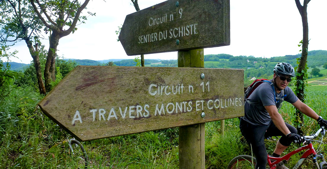 Un cycliste passe des paneaux de randonnée sur un petit chemin de foret