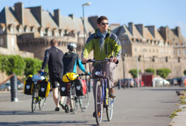 Cycliste à vélo croisant 2 cyclistes à pied devant les remparts de Saint Malo