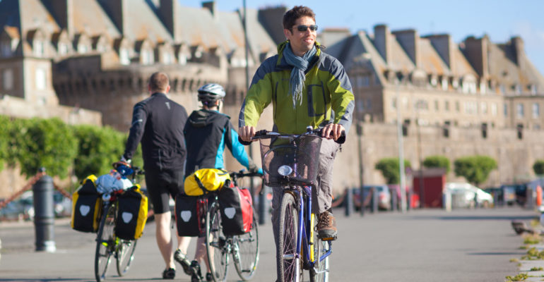 Cycliste à vélo croisant 2 cyclistes à pied devant les remparts de Saint Malo