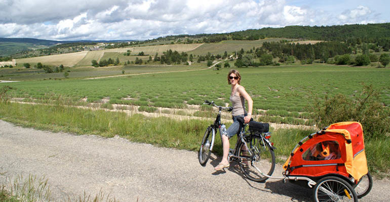 Femme sur son vélo avec une remorque pour enfant pose devant la campagne Le petit tour du Luberon