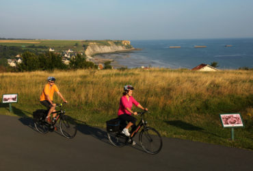 2 cyclistes avec au loin la plage d'Arromanches à vélo Normandie