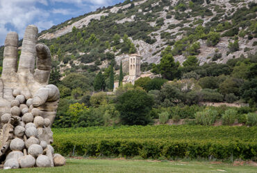 Une grande statue de pierre représentant une main tenant du raisin au milieu d'un vignoble