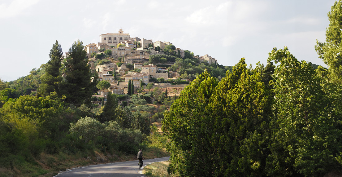 Un cycliste roule sur une route rejoignant le village perche de Gordes