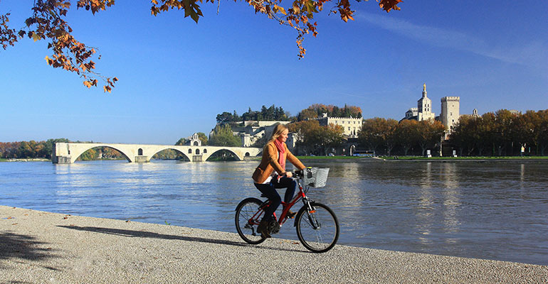 Cycliste le long du Rhône avec en arrière-plan le Pont et la ville d'Avignon, destination vacances à vélo en Provence