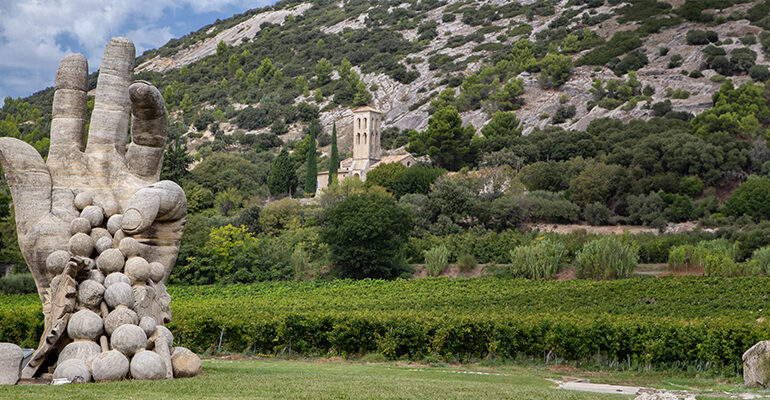 Une statue de main de vigneron tenant une grappe de raison au milieu des vignes