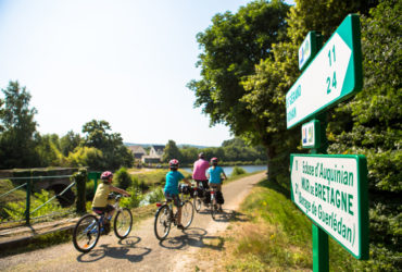 Famille de cyclistes pendant leurs vacances à vélo en Bretagne devant panneaux de direction itinéraire à vélo