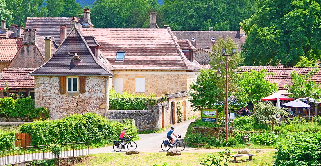 Un couple de cyclistes traverse un petit village de Dordogne