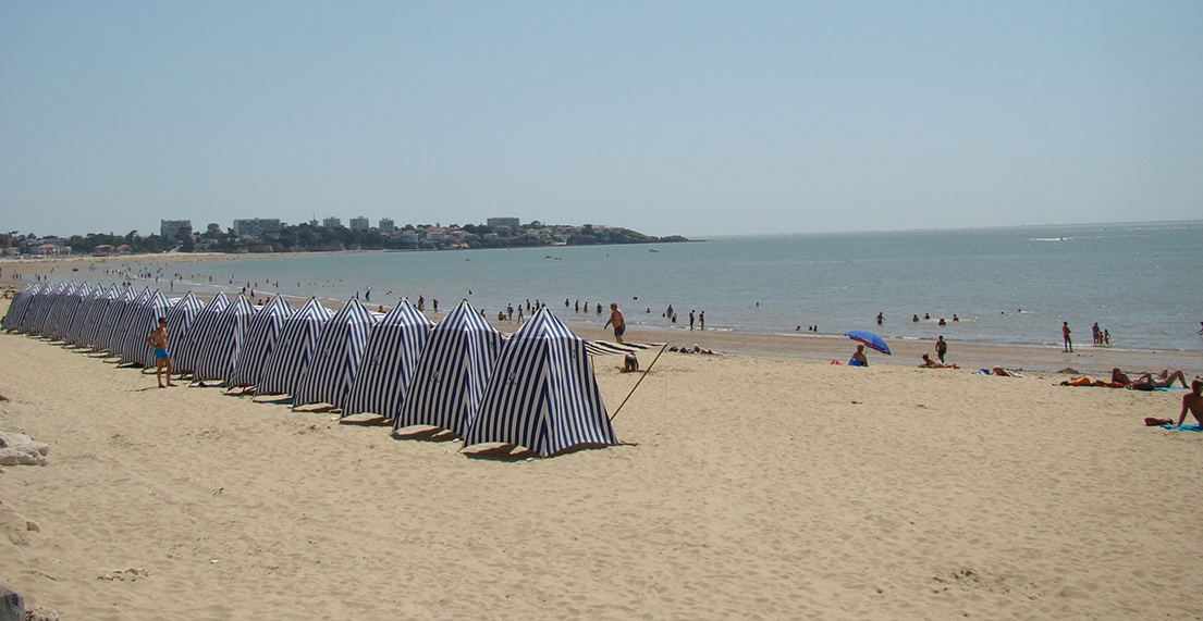 Une longe plage de sable fin avec des cabanes en tissu blanches et bleues