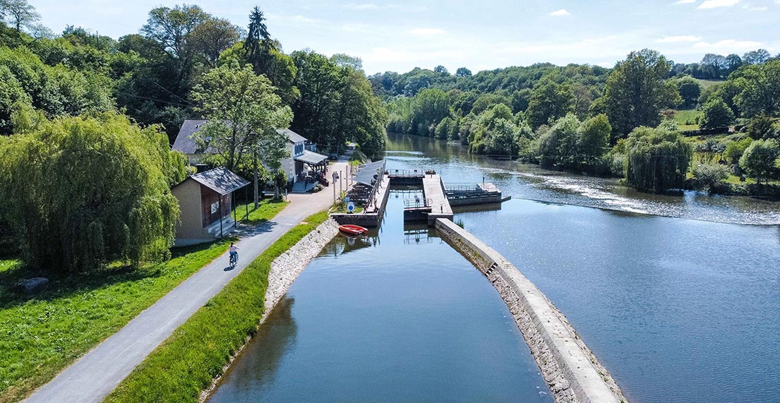 Une cycliuste roule le long d'un canal bordé de verdure