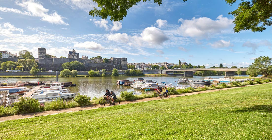 Un groupe de cycliste roule le long d'un canal bordé par la ville d'Angers
