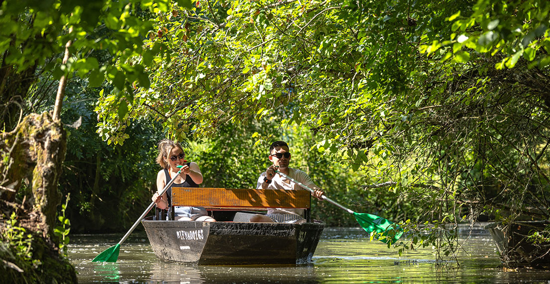 Un couple pagaie dans une barque entourée de verdure