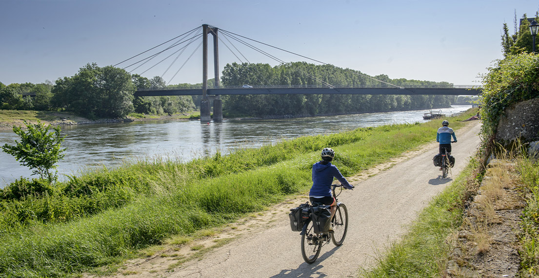 Un couple de cyclistes roule le long de la Loire sur un chemin de halage blanc entouré de verdure