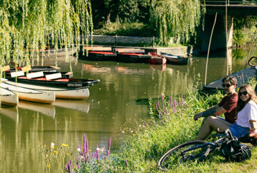Un couple de cyclistes se repose devant un canal avec des barques
