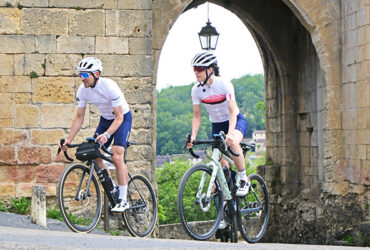 Un couple de cyclistes sur route traverse un village de pierres