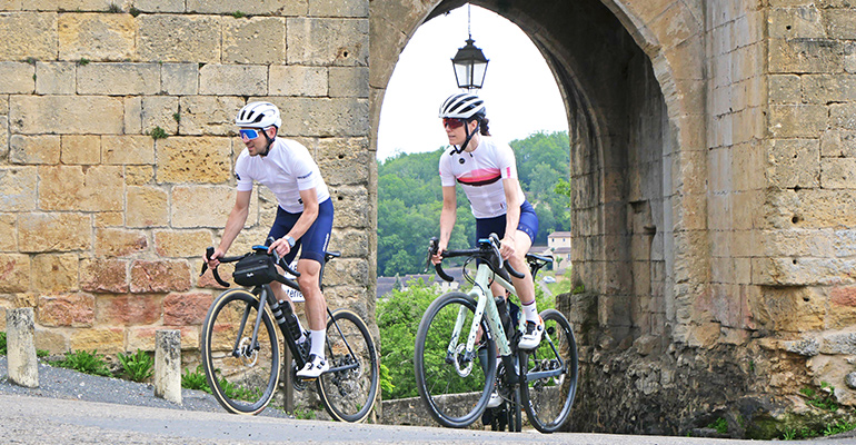 Un couple de cyclistes sur route traverse un village de pierres