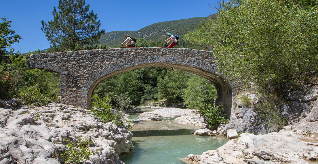 Deux cyclistes traversent un pont de pierres