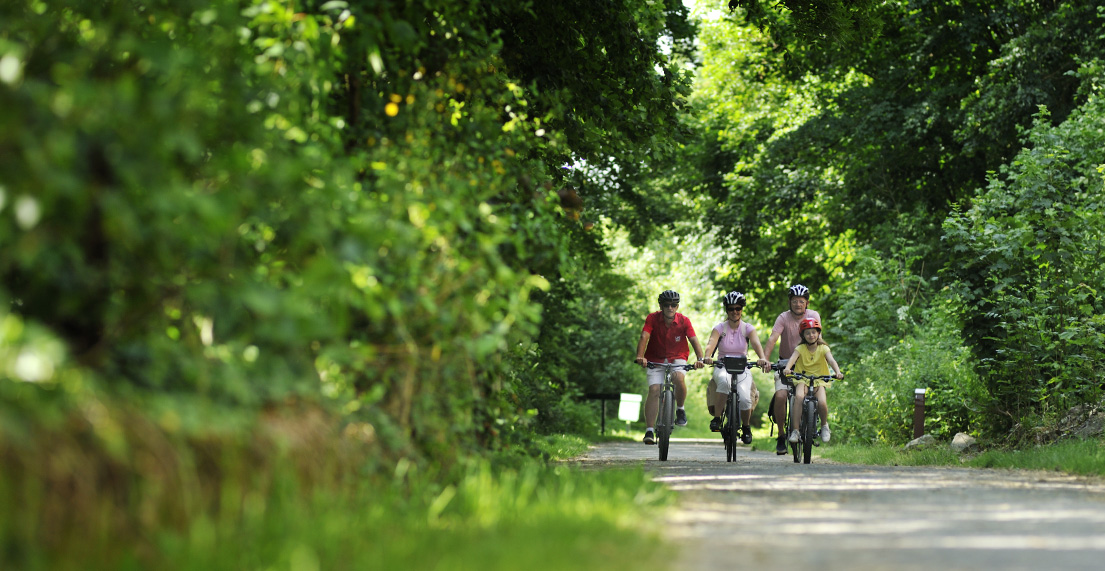 Une famille de cycliste roule sur un chemin de halage entouré de verdure