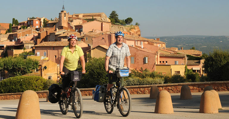 Couple à vélo en danseuse à la sortie d'un village Le petit tour du Luberon