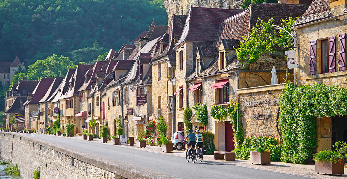 Un couple de cycliste roule devant les maisons troglodytes de La Roque-Gageac