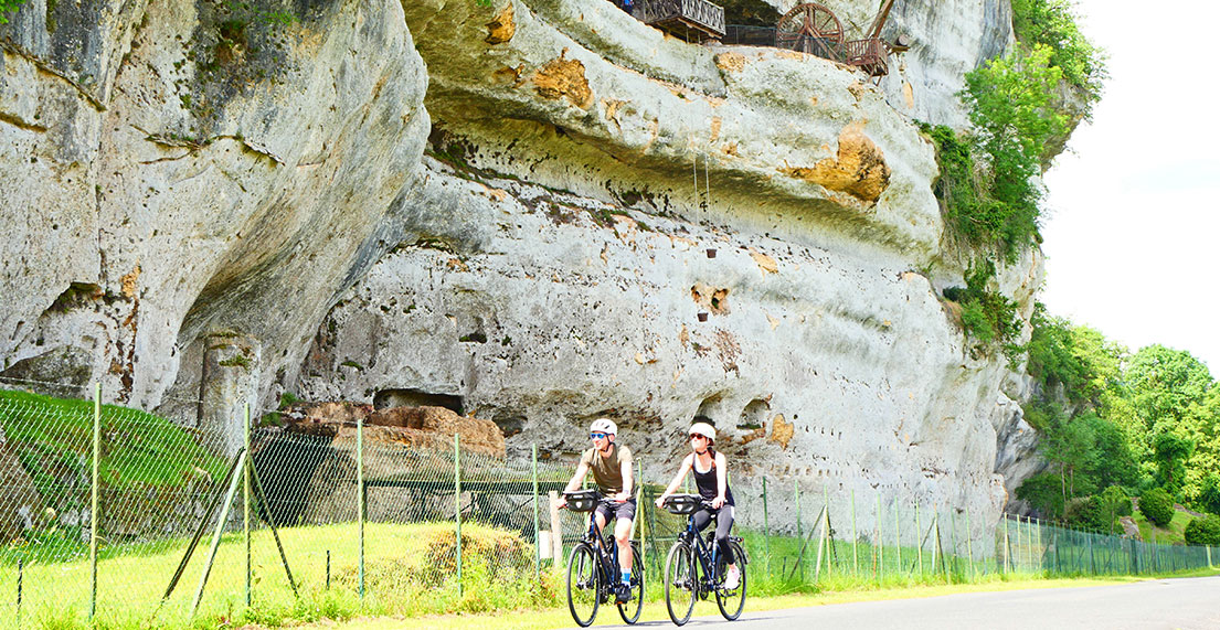 Un couple de cycliste roule devant les falaise de calcaire des Eyzies